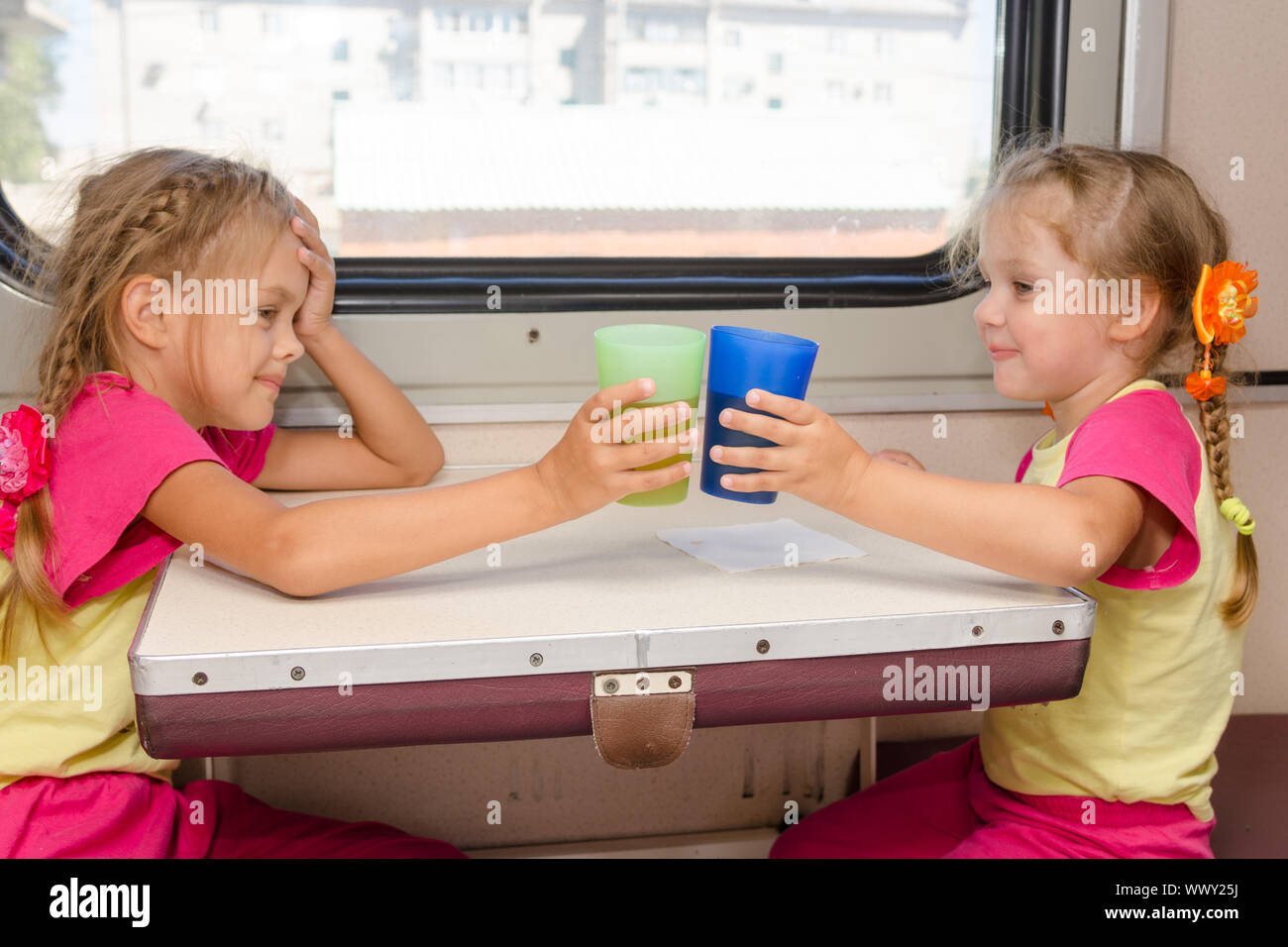 Due piccole sorelle in identiche pigiami bere il tè in treno al tavolo su esterno della seconda classe di trasporto Foto Stock