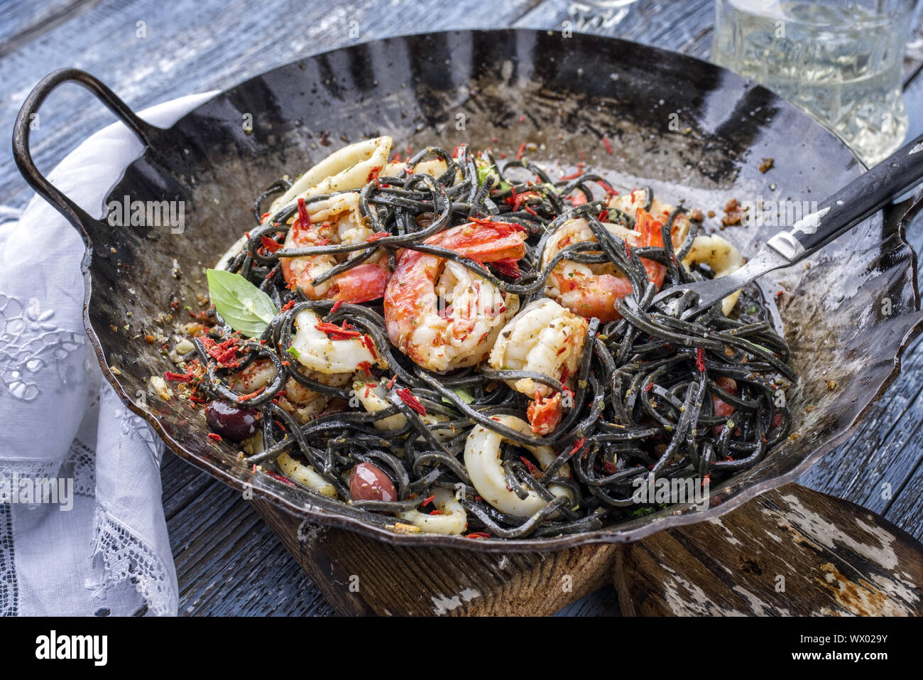 Italian linguine con tinta de i calamari e scampetti con olive come close-up di un adirato padella di ferro Foto Stock