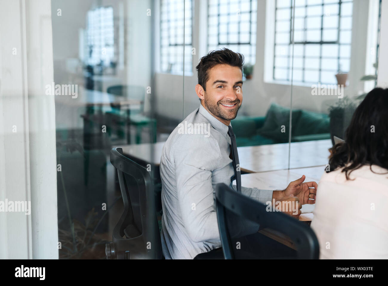 Sorridente imprenditore giovane seduto con i colleghi in una sala riunioni Foto Stock