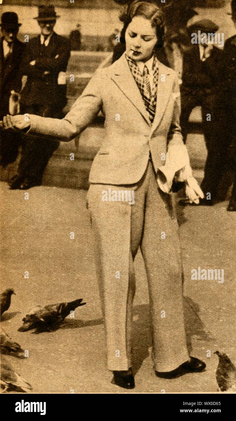 "Una signora betrousered alimentare piccioni in Trafalgar Square", 1933. Il fumo donna che indossa un pantalone-vestito in centro a Londra. Questo stile di abito è diventato sempre più popolare e socialmente accettato - in questo momento: durante il XIX secolo, le donne occidentali potrebbe essere arrestato per indossare i pantaloni. Da "il corteo del secolo". [Odhams Press Ltd, 1933] Foto Stock