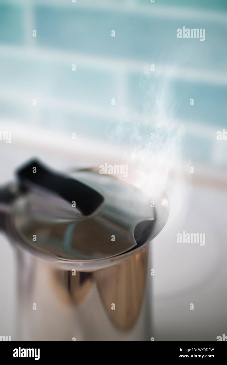 Bollitore per il tè con acqua bollente contro una mattonella blu in cucina Foto Stock