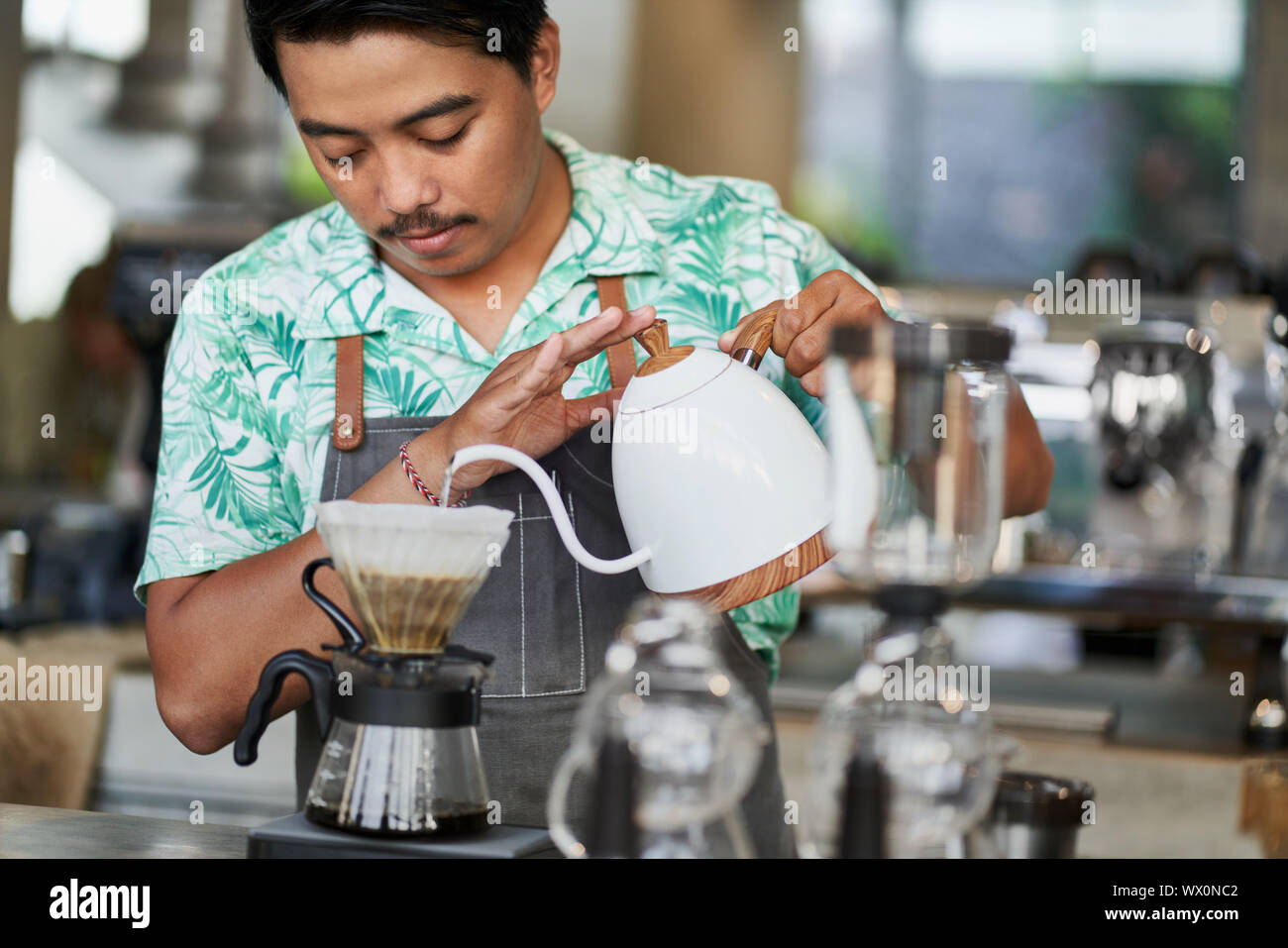 Schietto stile di vita colpo di sorridente indonesiano etnica barista e proprietario di piccola impresa la preparazione di organic fair-trade caffè nella luminosa trendy coffee shop Foto Stock