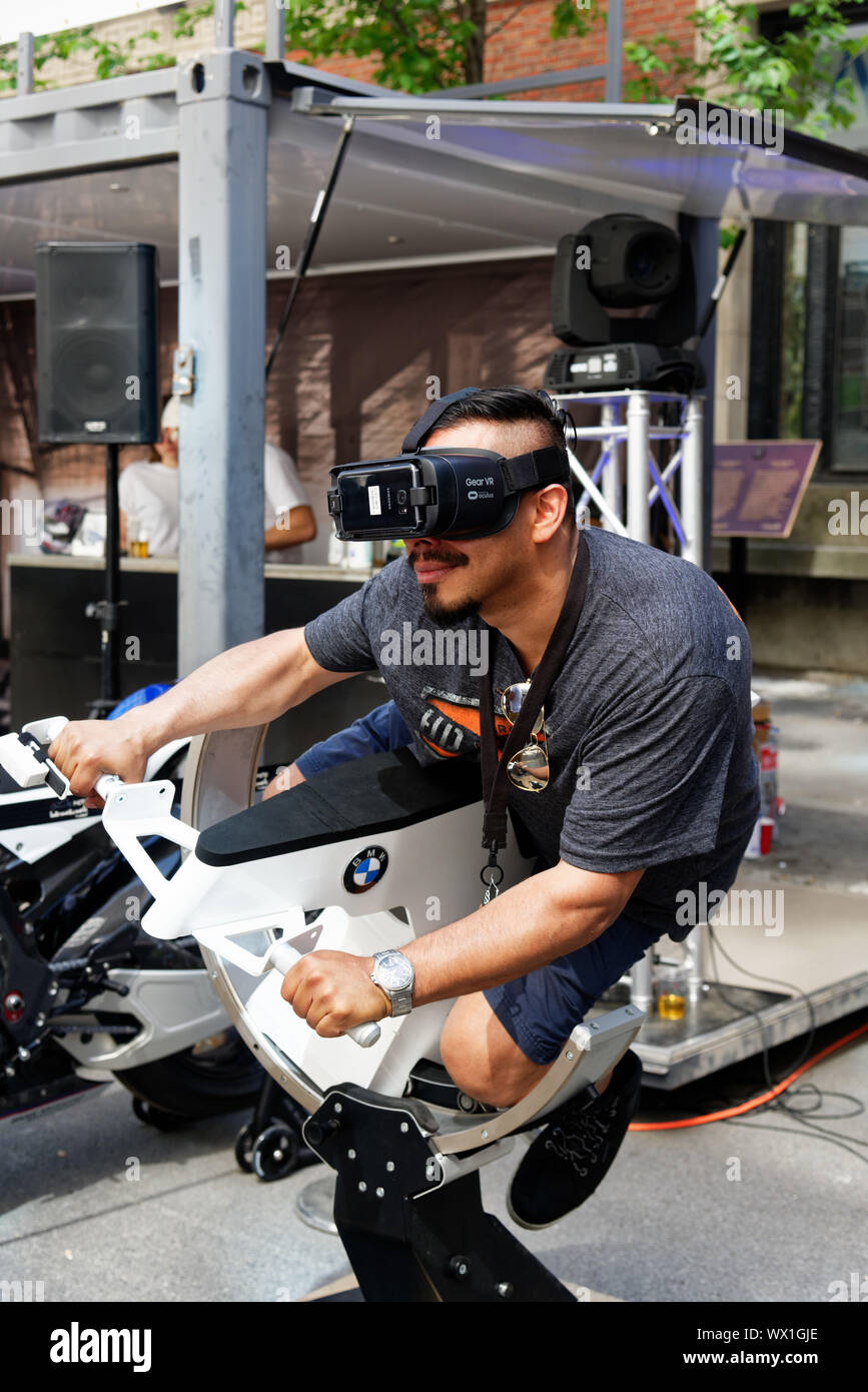 Un uomo che indossa la realtà virtuale gli occhiali e a cavallo di un simulatore di moto Foto Stock