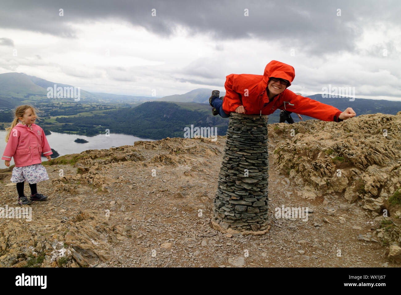 Una donna che finge di essere superman sul vertice del gatto campane nel distretto del lago mentre la figlia guarda su Foto Stock