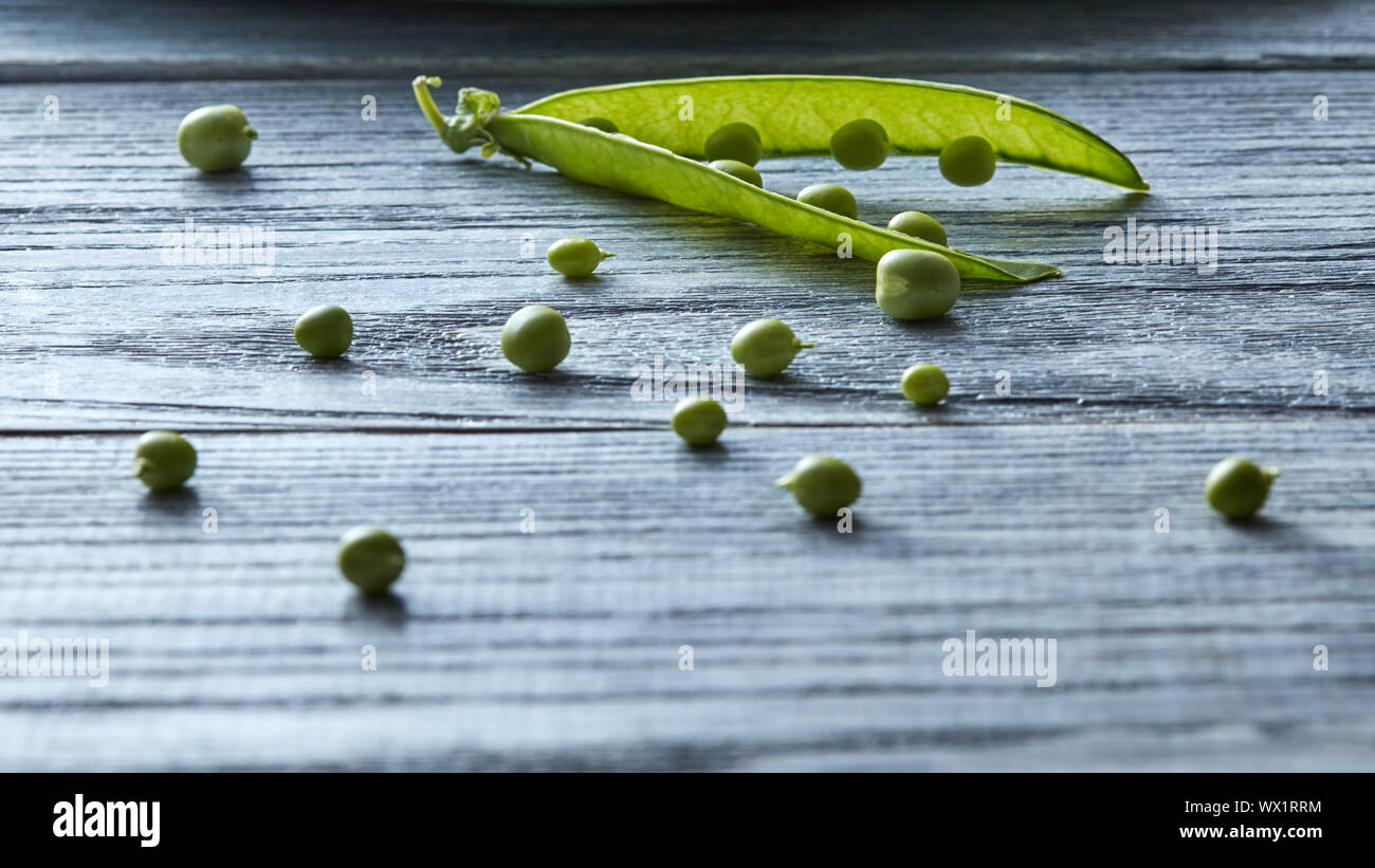 Verde biologico cialde di giovani piselli verdi aperto sul grigio di un tavolo di legno - ingrediente per la cottura di insalata. Foto Stock