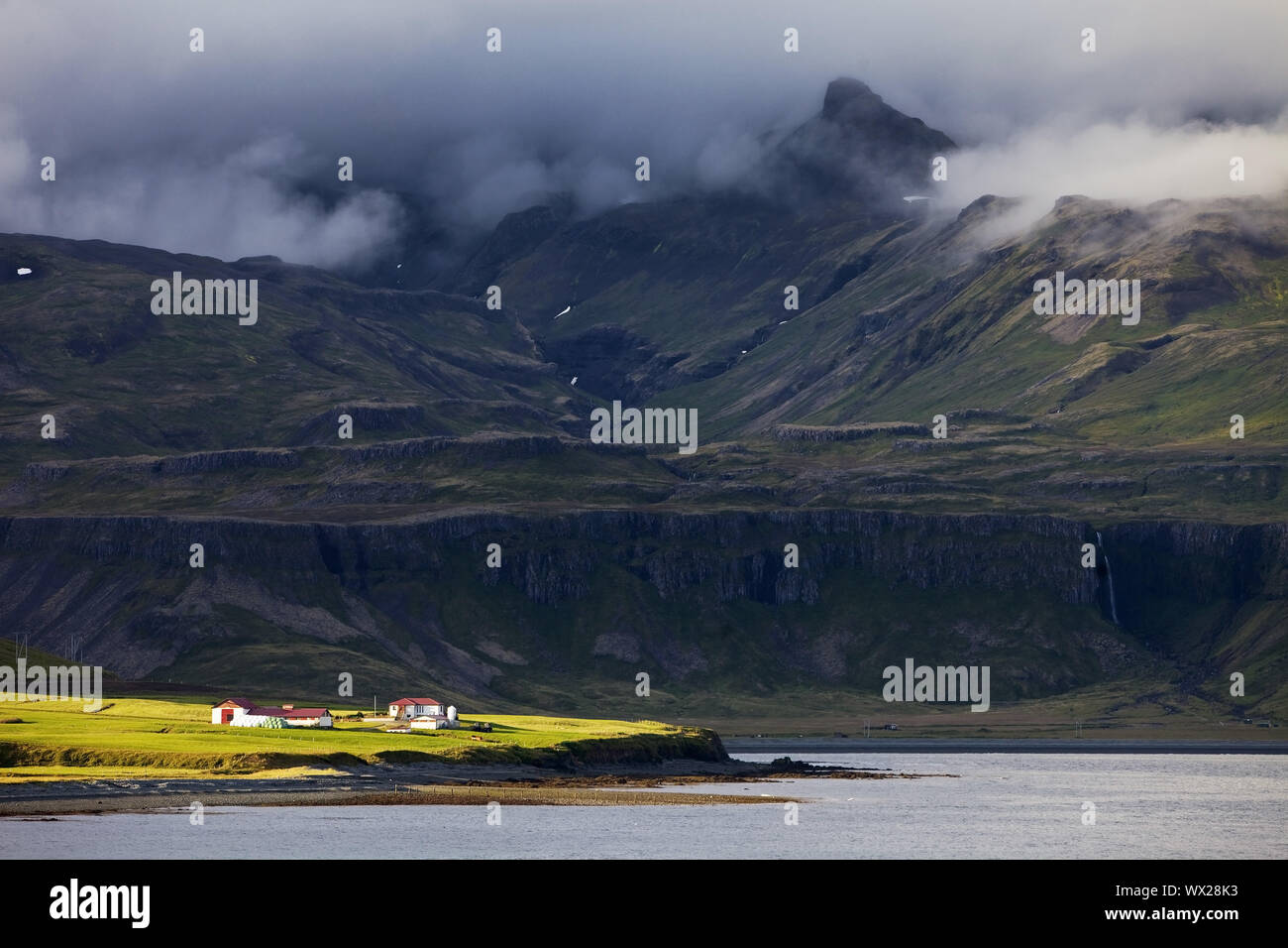 Paesaggio vicino Grindafjoerdur con la fattoria nel sole di fronte montagne scure, Snaefellsnes, Islanda Foto Stock