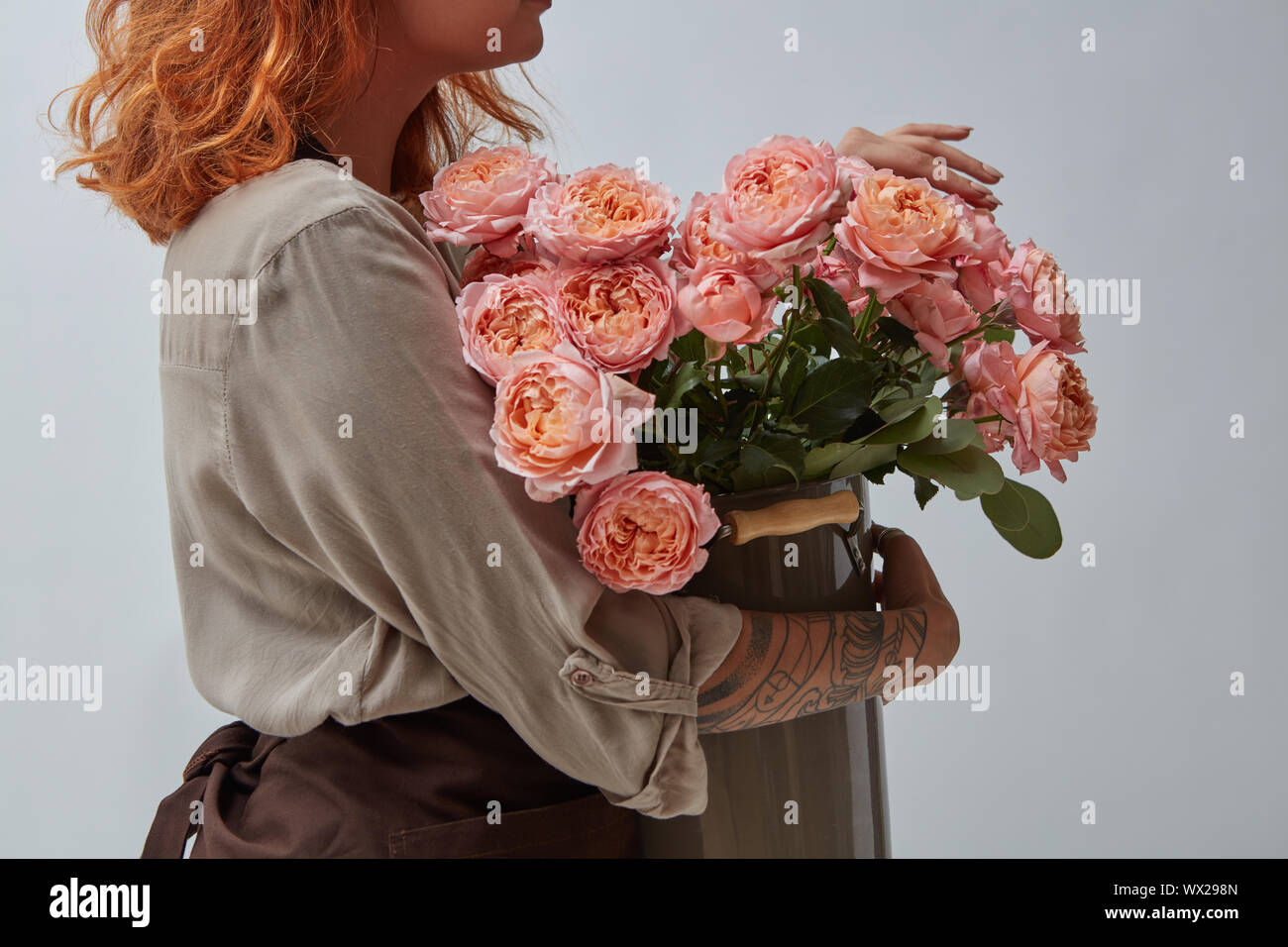I Capelli rossi ragazza fioraio tenendo un bouquet di rose rosa in un vaso su uno sfondo grigio con copia spazio. Il concetto di un fiore Foto Stock