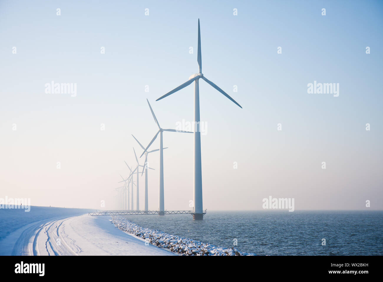 Fila di mulini a vento nevoso in piedi nel mare olandese di scomparire in inverno haze Foto Stock