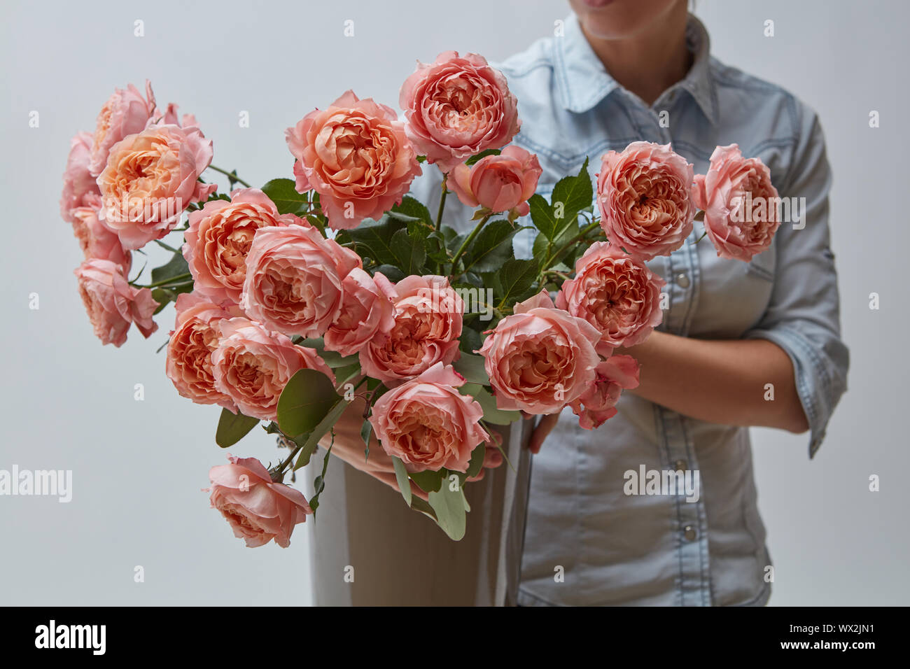 Un profumo di rosa fresca Rose in un vaso marrone detiene una ragazza nelle sue mani Foto Stock