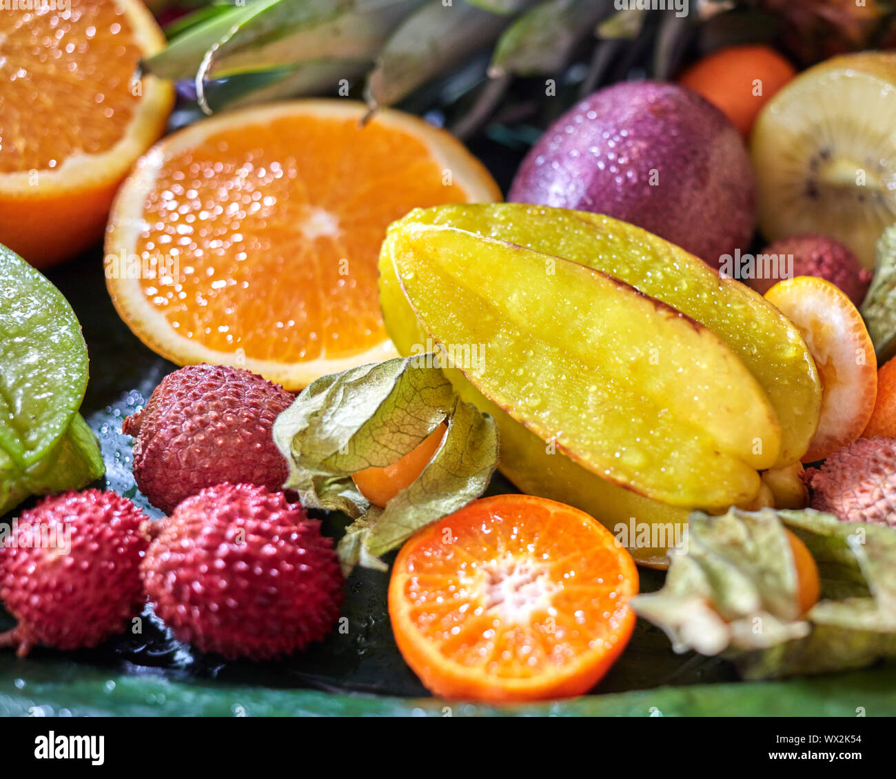 Succosa fresca frutta tropicale come un backgraund. Carambole, litchi, kumquat, arancione metà, phisalis su foglie verdi. Close-up. Foto Stock