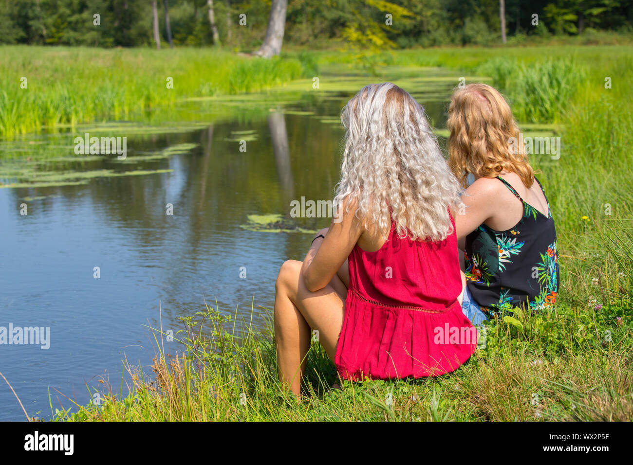 Due giovani donne siedono insieme a waterfront Foto Stock