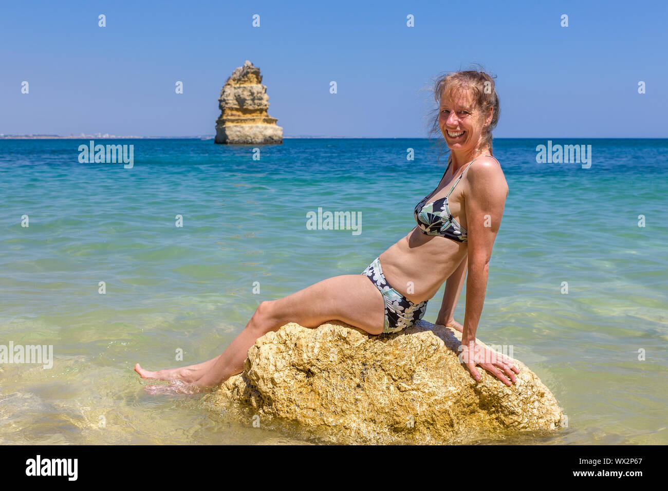 Donna che indossa un bikini si siede sulla roccia in mare Foto Stock