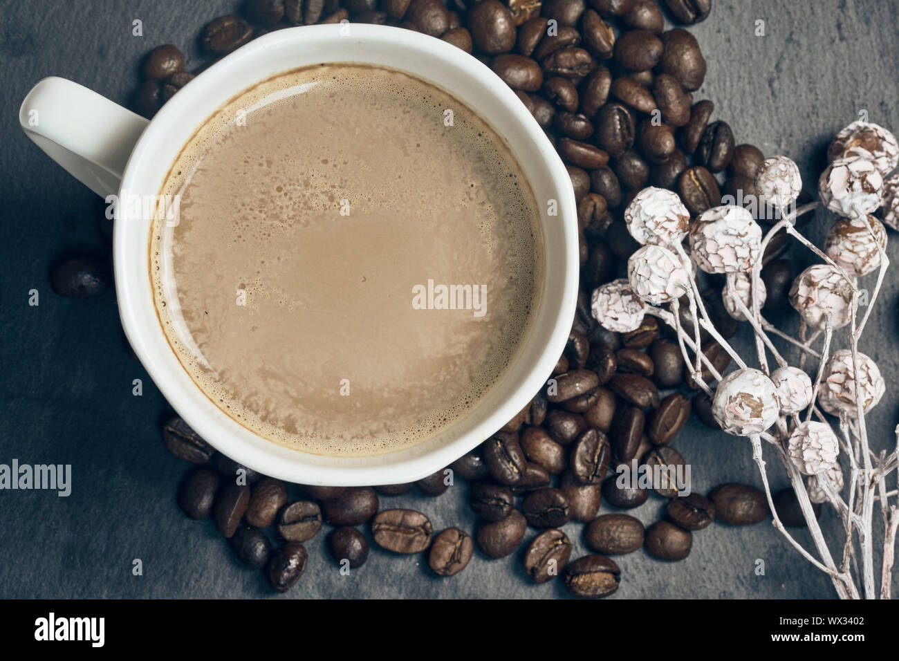 Vista superiore del caffè caldo in una tazza bianca con chicchi di caffè tostati e autunno decorazione su sfondo di ardesia Foto Stock