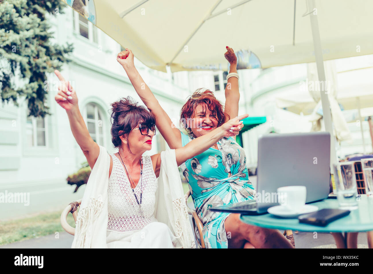 Due entusiasti le donne anziane la lettura di buone notizie on line con un laptop in outdoor cafe. Foto Stock
