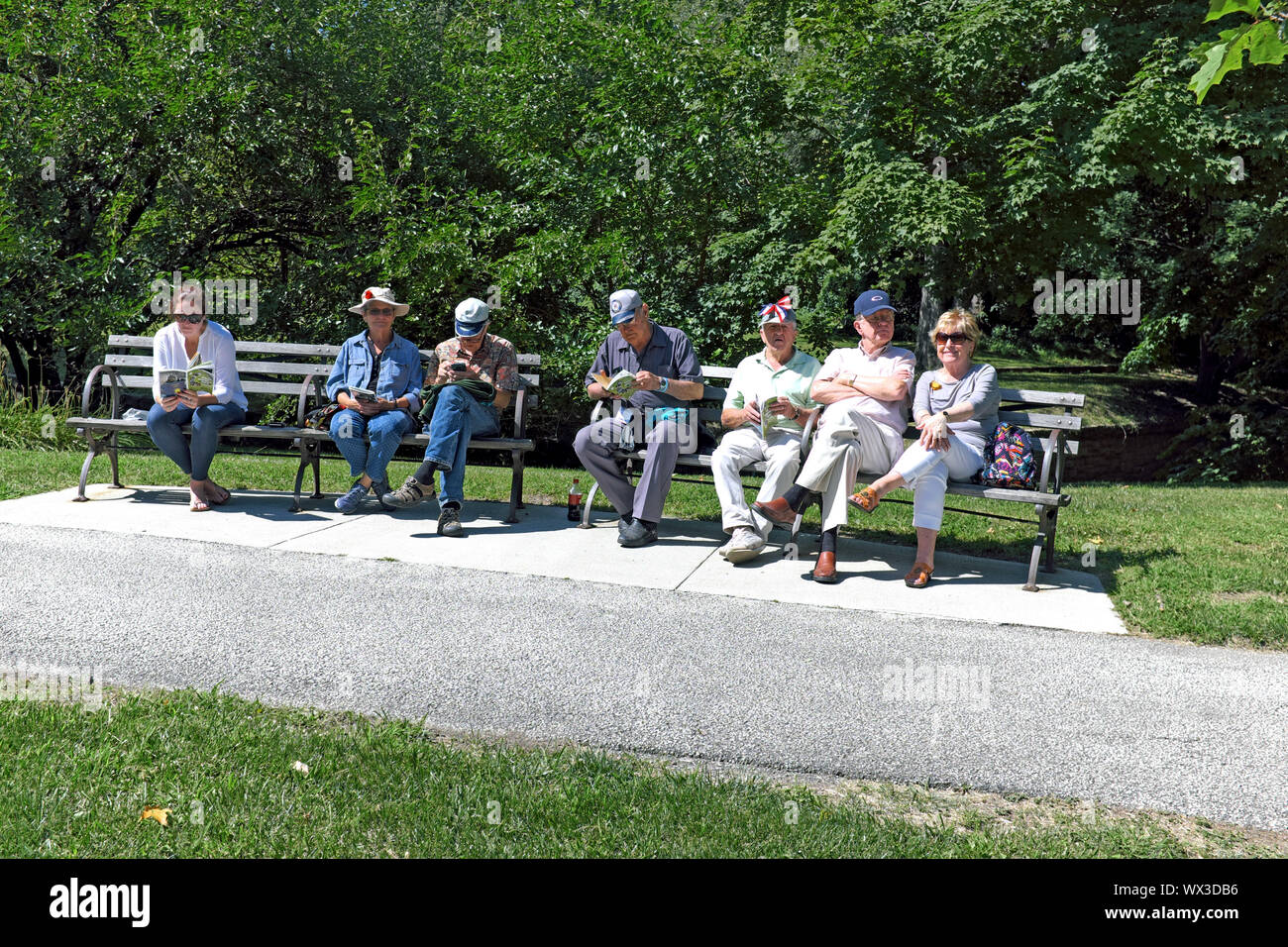 Sette persone, uno più giovani e per il resto i vecchi, condividere panchine nei giardini culturale di Rockefeller Park in Cleveland, Ohio, USA. Foto Stock
