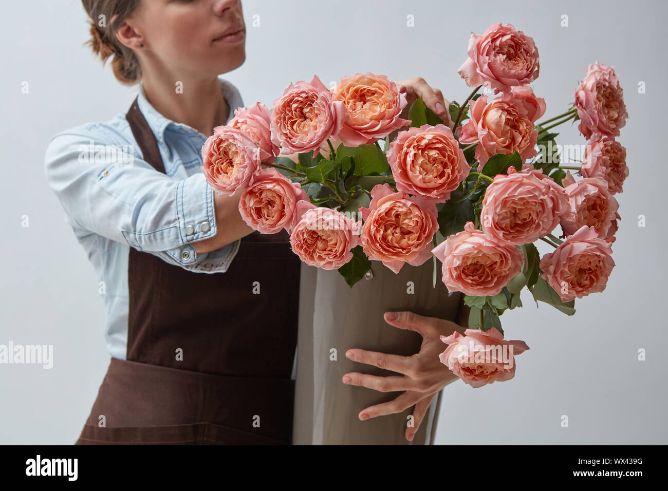 Ragazza fioraio con un grande mazzo di rose rosa intorno a uno sfondo grigio. Il concetto di un negozio di fiori Foto Stock