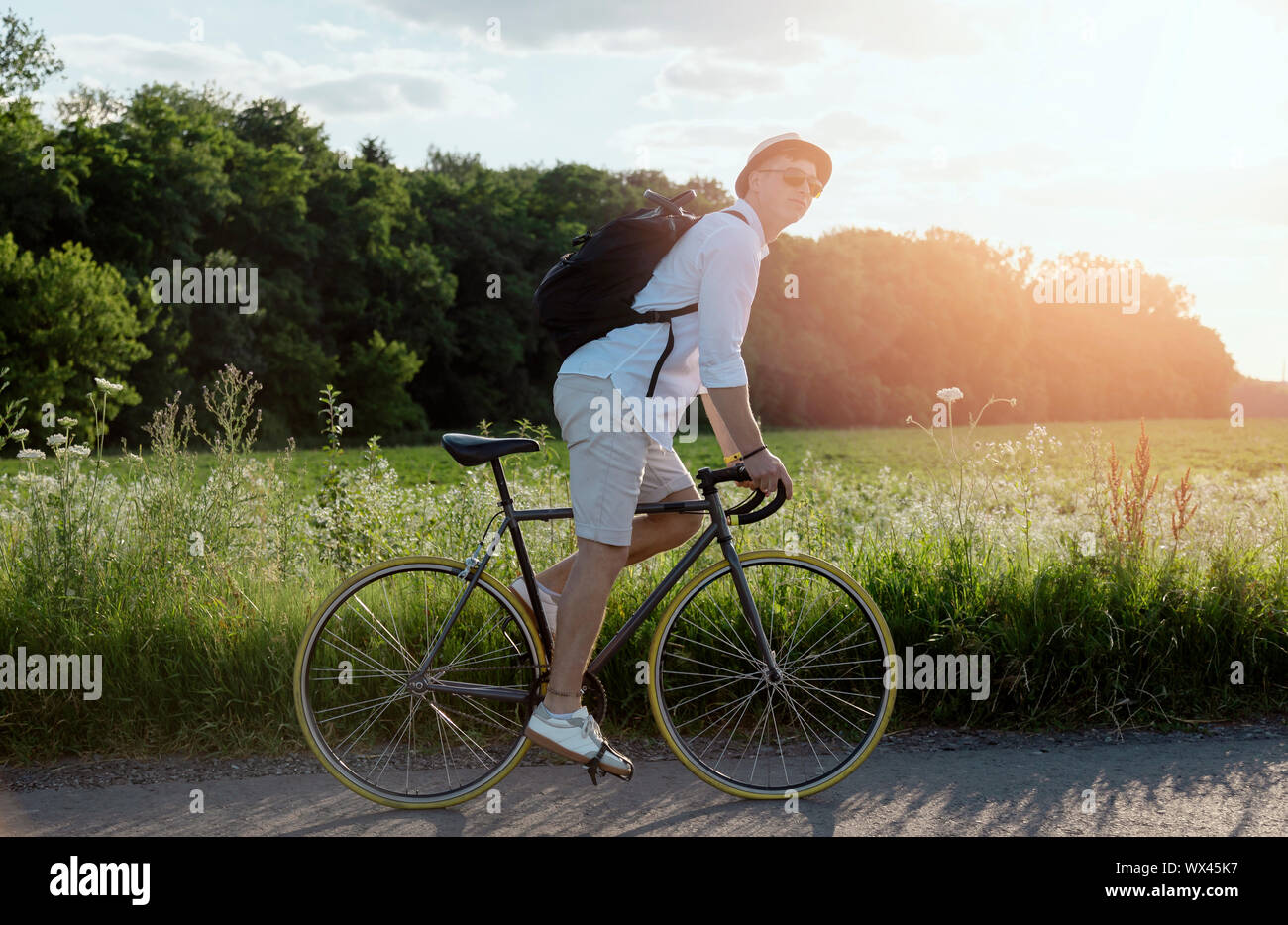 Giovane uomo in bianco indossando occhiali da sole godendo il suo rural viaggio in bicicletta Foto Stock