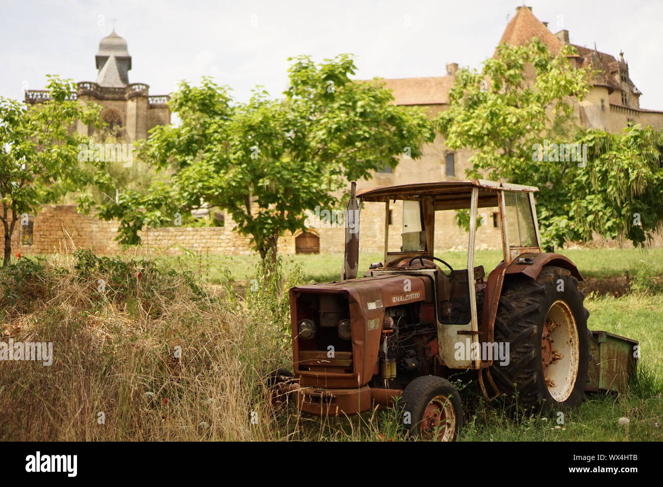 Un rosso vecchio arrugginito trattore parcheggiato in una fattoria orchard nelle zone rurali in Francia con il villaggio in background Foto Stock