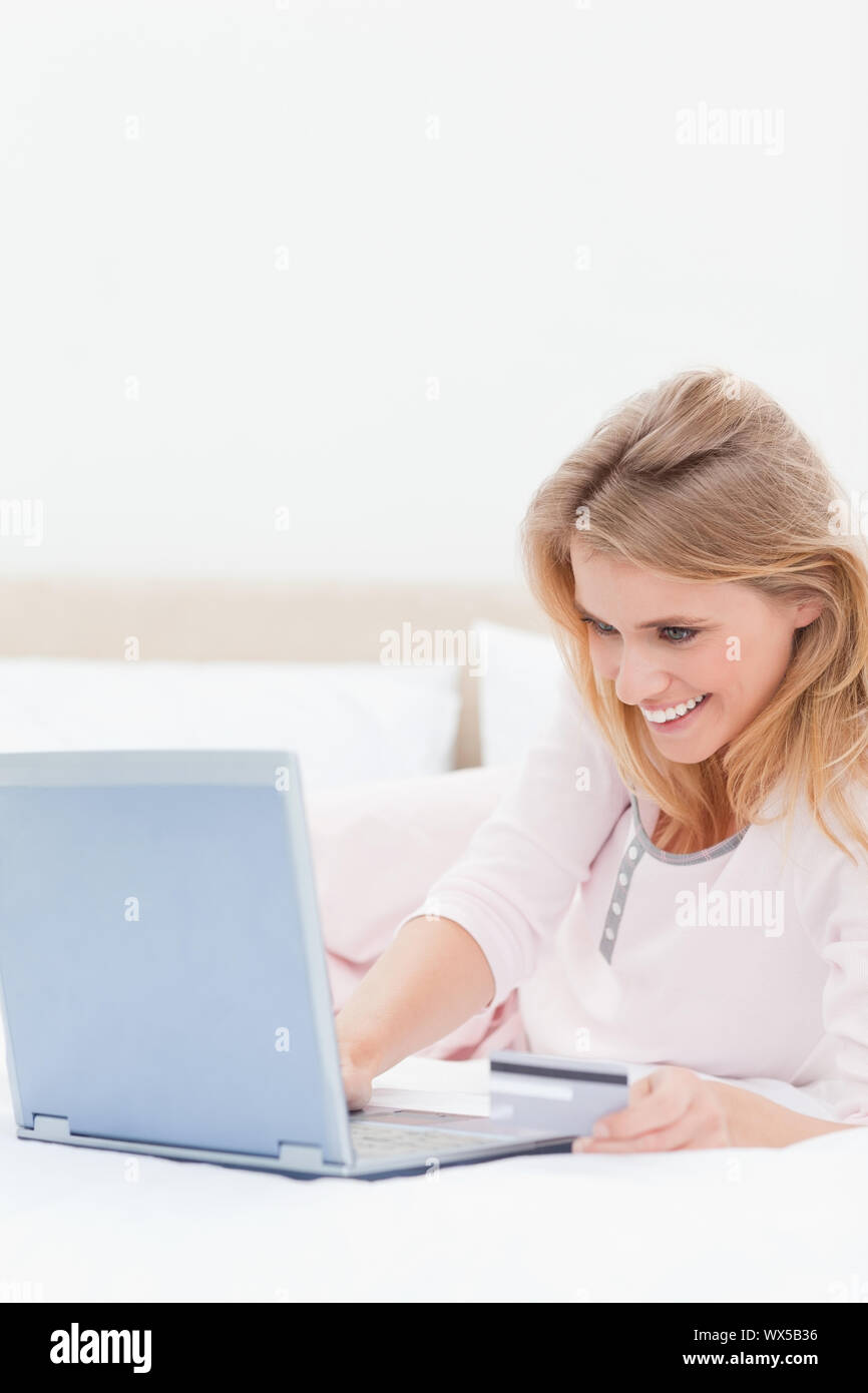 Un'immagine ravvicinata di una donna sorridente che guarda al suo laptop come lei giace sul suo letto. Foto Stock