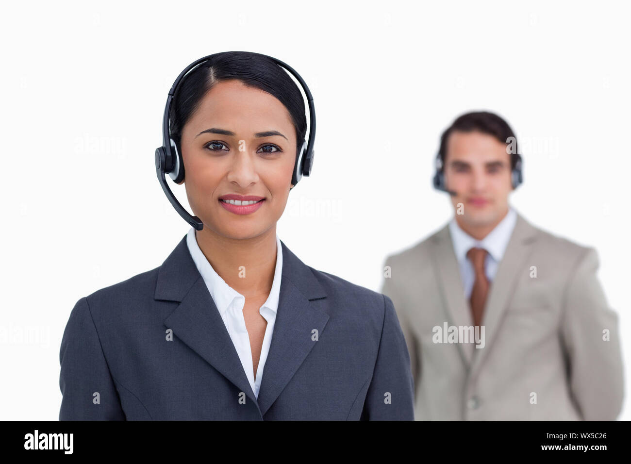 Sorridente supporto telefonico lavoratore con il collega dietro di lei contro uno sfondo bianco Foto Stock