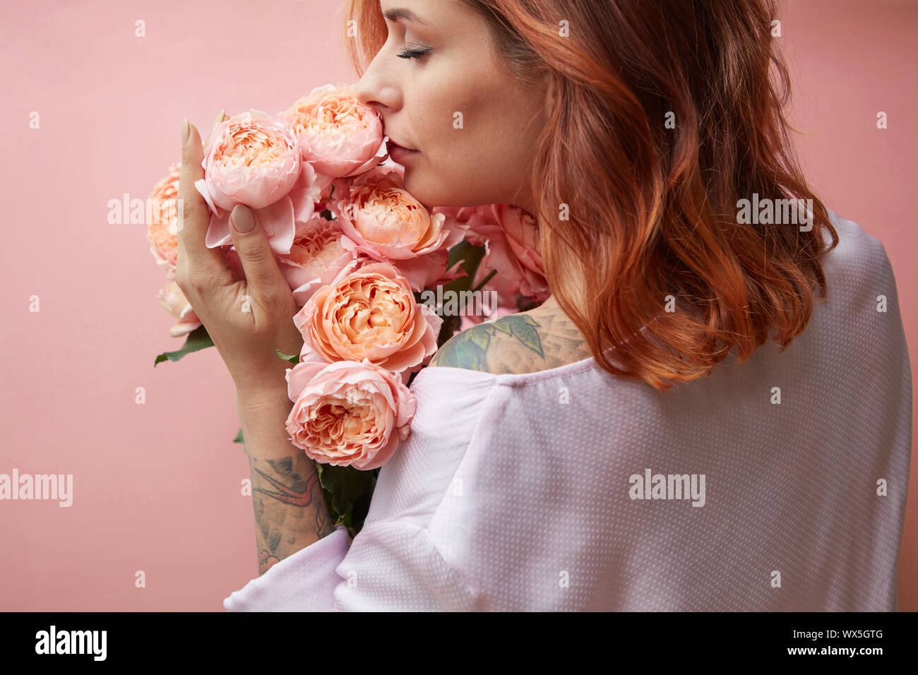 Una ragazza con un tatuaggio tiene un mazzo di fiori di rose su uno sfondo color pastello in un colore alla moda del 2019 coralli viventi Pan Foto Stock