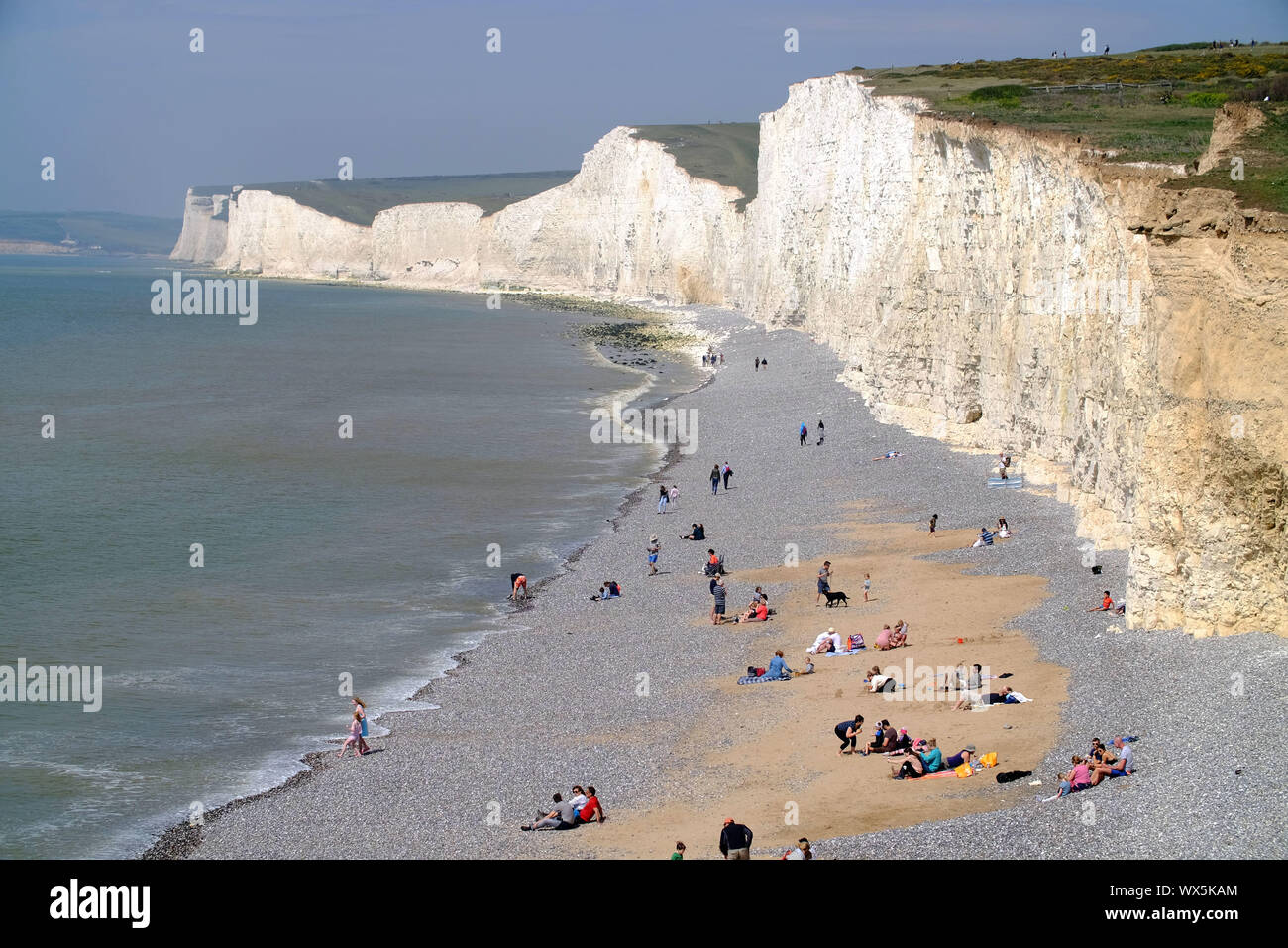I turisti sulla spiaggia di Birling Gap, sotto l'iconica sette sorelle chalk cliffs. East Sussex, Regno Unito Foto Stock