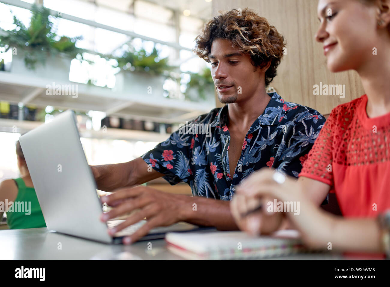 Schietto stile di vita colpo di attraente multi-etnico millenario di pianificazione dei colleghi sul computer allo stand del moderno e luminoso tanga tropicale cafe Foto Stock