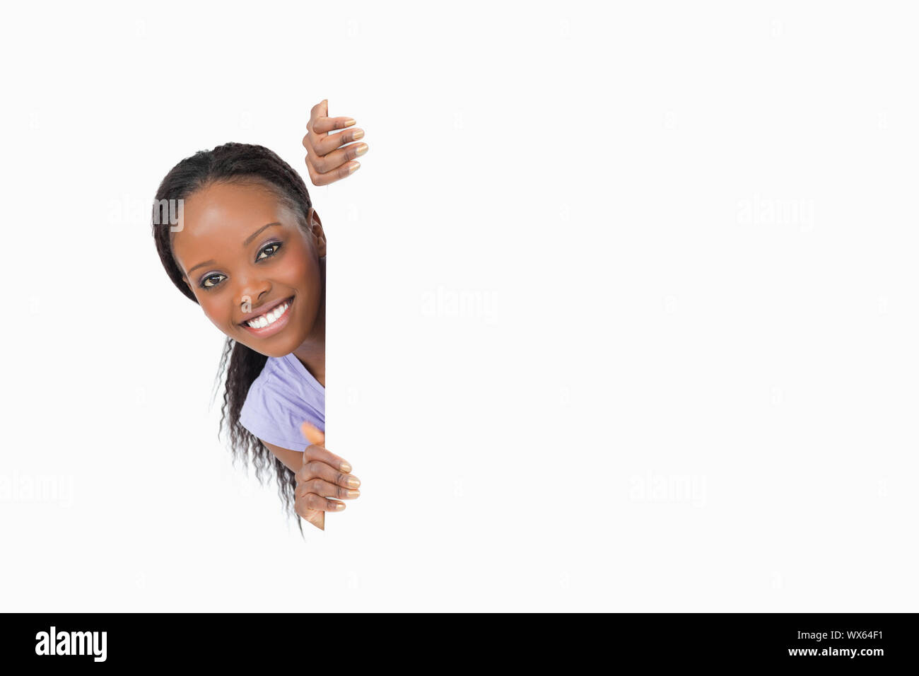 Donna sorridente di dare una occhiata dietro l'angolo su sfondo bianco Foto Stock