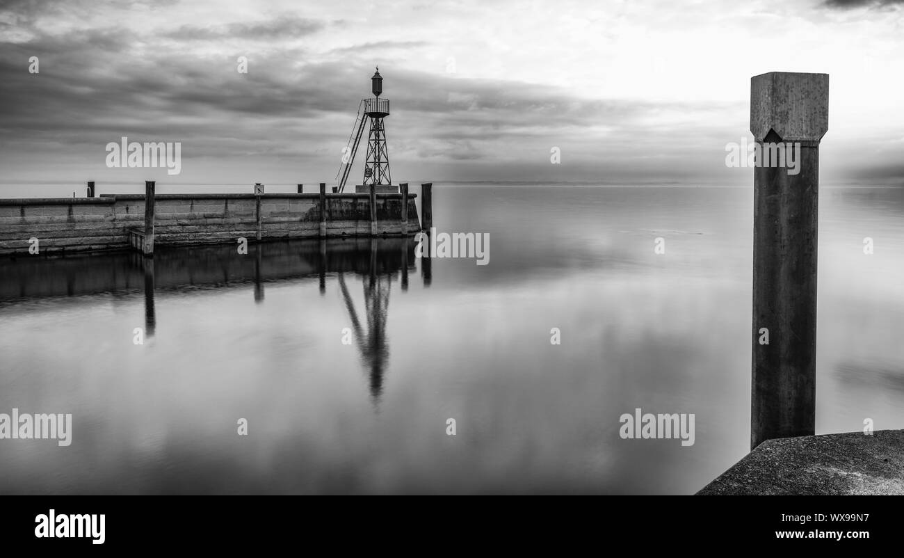 La luce di segnale e di parete di porto sulle calme acque del lago sotto un cielo nuvoloso lo spazio negativo abstract Foto Stock