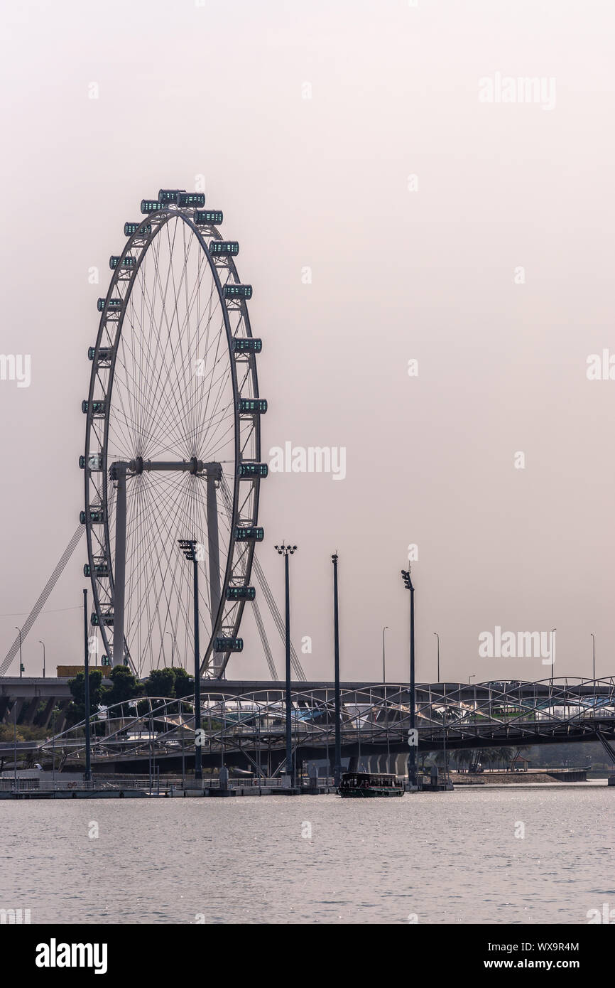 Singapore - Marzo 21, 2019: primo piano dello Flyer ruota panoramica Ferris di Marina Bay contro il cielo grigio. Acqua marina nella parte anteriore e un ponte pedonale. Foto Stock