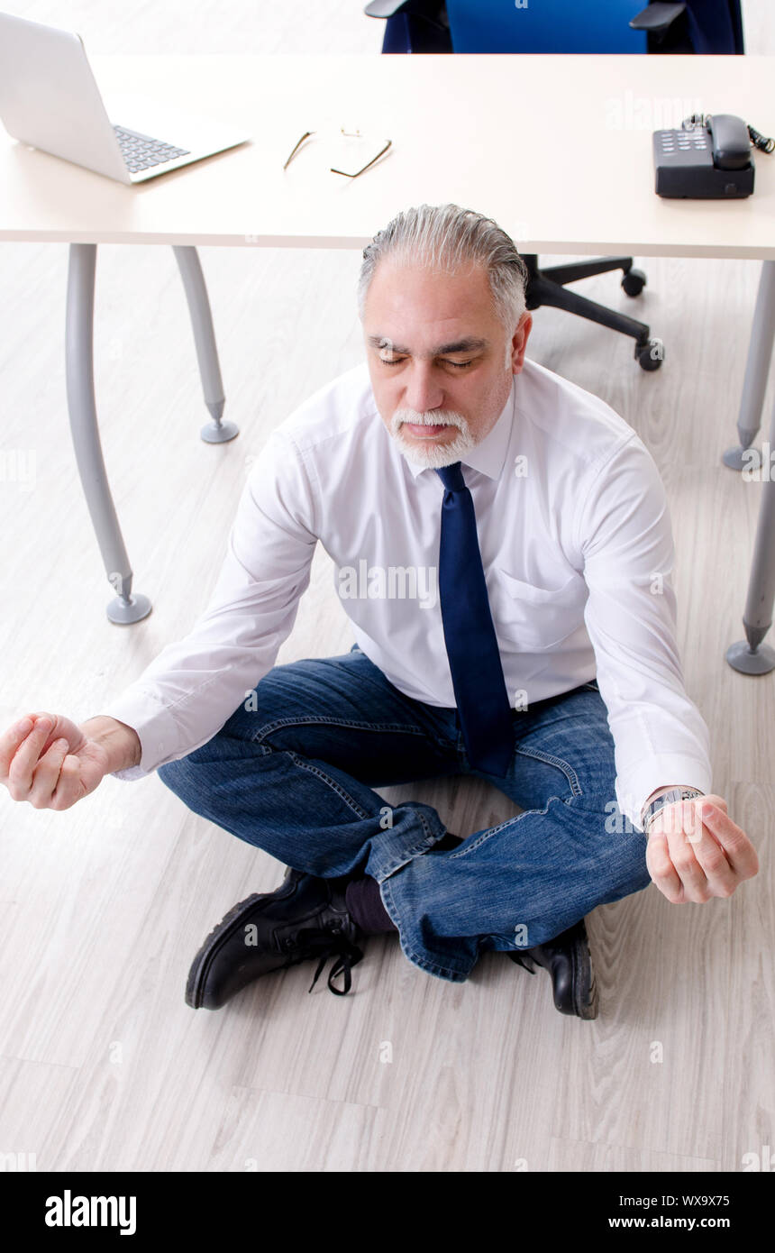 Imprenditore invecchiato facendo esercizi yoga in ufficio Foto Stock