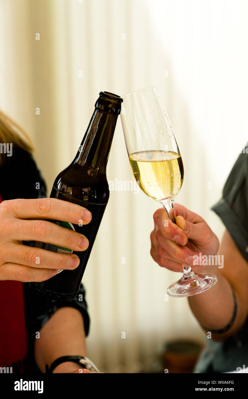 Due donne che fanno un brindisi con una bottiglia di birra e un bicchiere di champagne Foto Stock