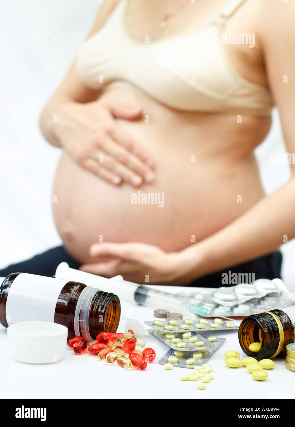Giallo e rosso pillole fuoriuscita dalle bottiglie e blister nella parte anteriore della donna incinta, shallow DOF Foto Stock