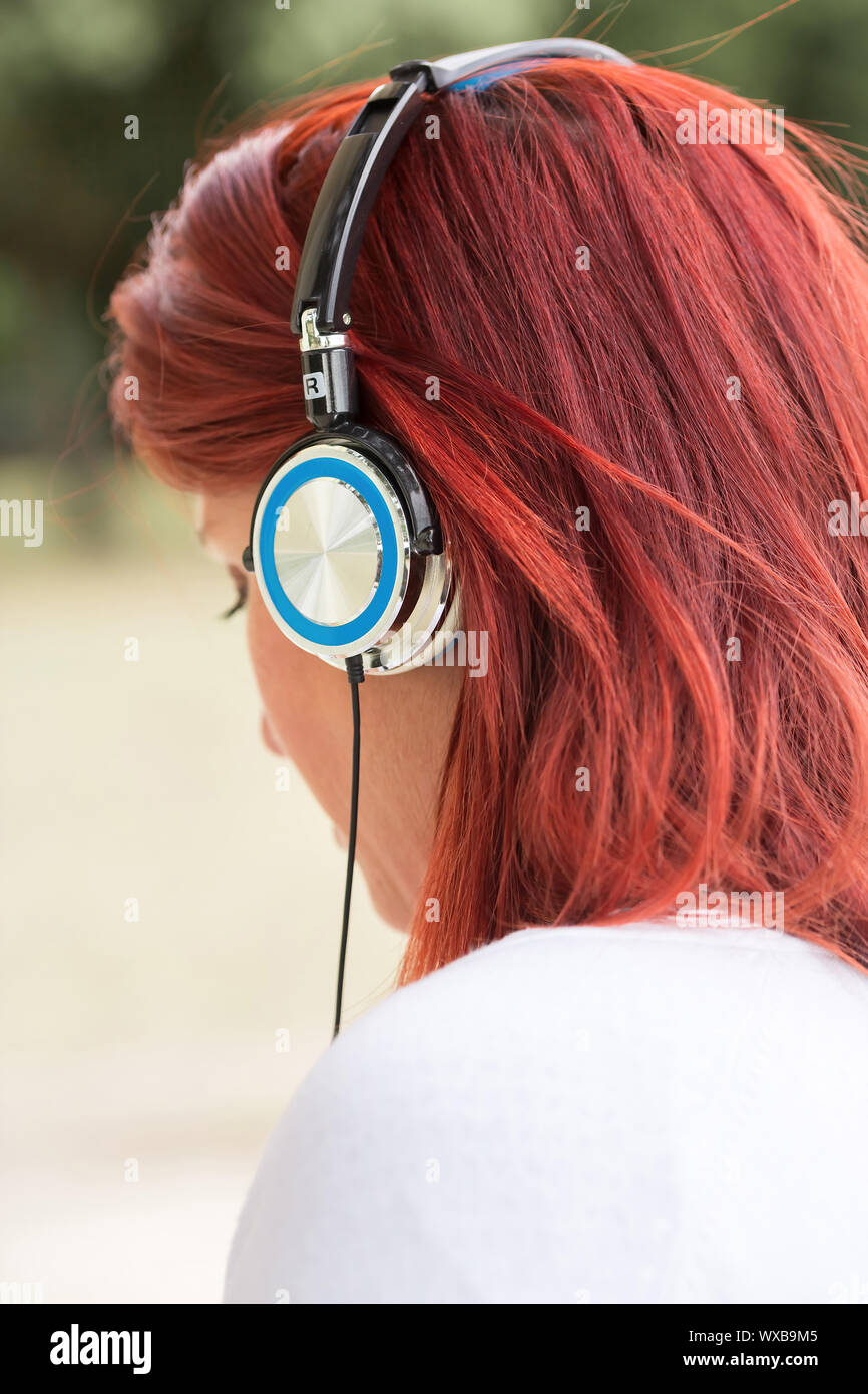 Ritratto di donna redhead ascoltando musica in cuffia con verde in background Foto Stock