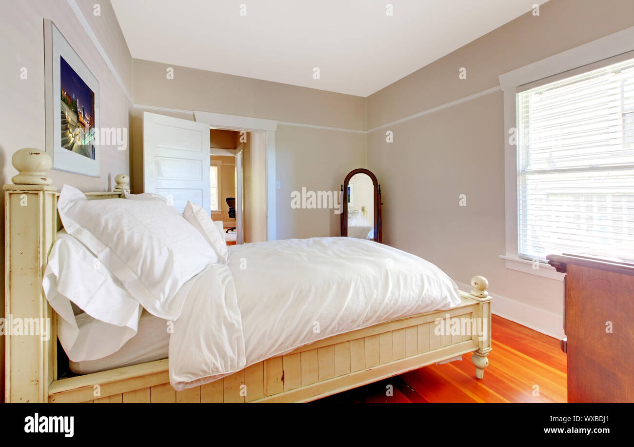 Luminosa camera da letto con letto bianco e pareti beige e pavimento di legno. Foto Stock