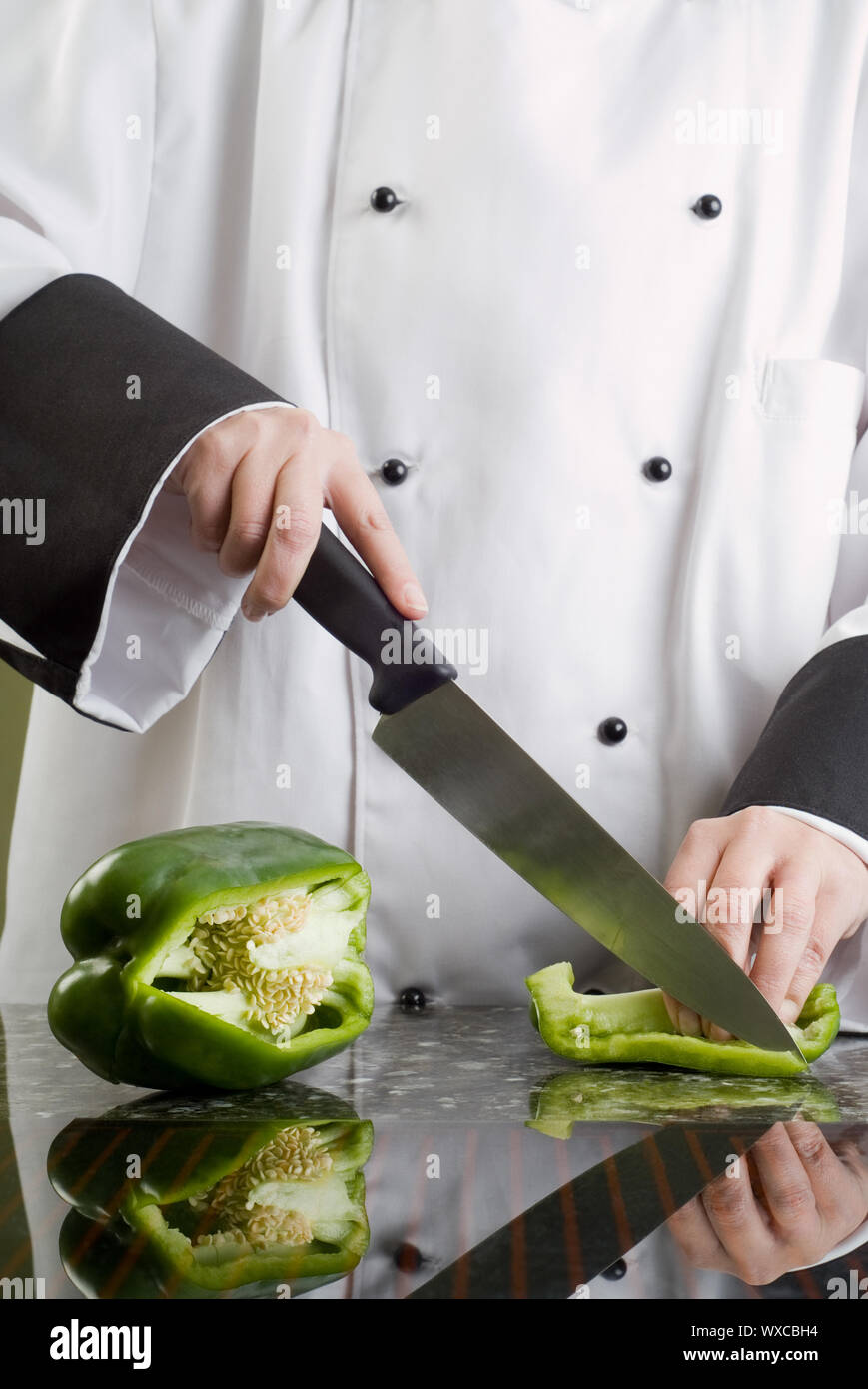 Chef in bianco e nero di taglio uniforme un peperone verde riflettendo in stufa Top Foto Stock