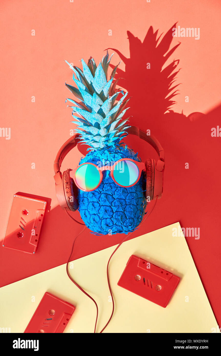 Funny ananas in occhiali da sole e auricolari con retrò nastri audio. Appartamento giaceva sul corallo, di colore arancione e rosso sfondo della carta con un'ombra. Foto Stock