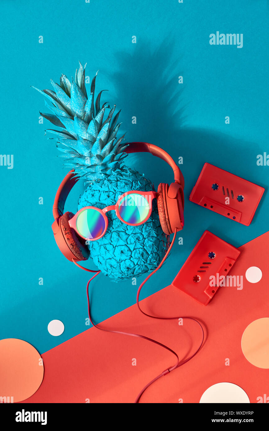 Funny ananas in occhiali da sole e auricolari con un'ombra, piatto stendere sui blu e rosso sfondo della carta Foto Stock