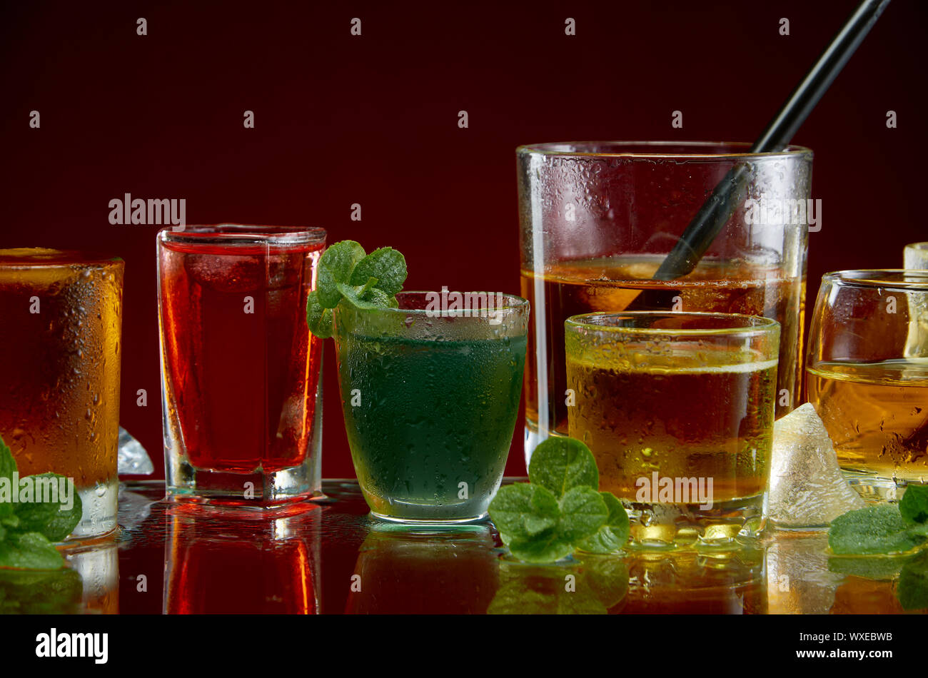 Vari cocktail alcolico in chiaro bicchieri con ghiaccio e menta su uno sfondo rosso Foto Stock