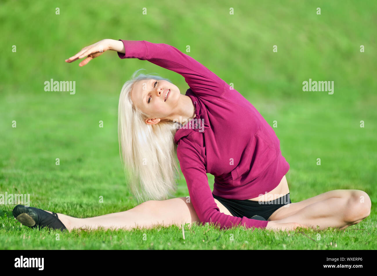 Bella giovane donna facendo esercizio di stiramento su erba verde al parco. Lo Yoga Foto Stock