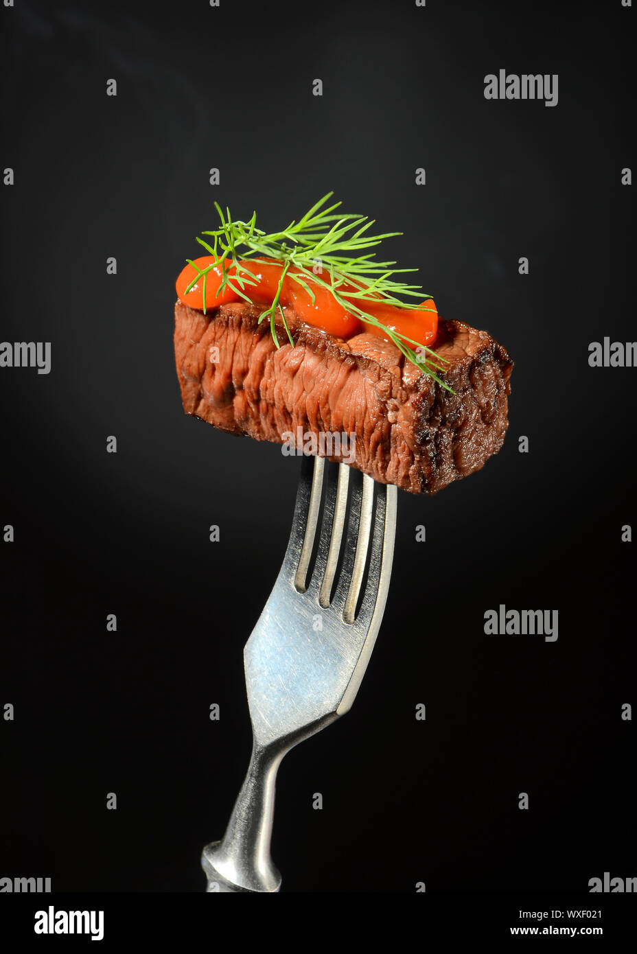 Un succoso pezzo di carne con ketchup e aneto è piantato su una forcella su sfondo scuro con il fumo. Foto Stock