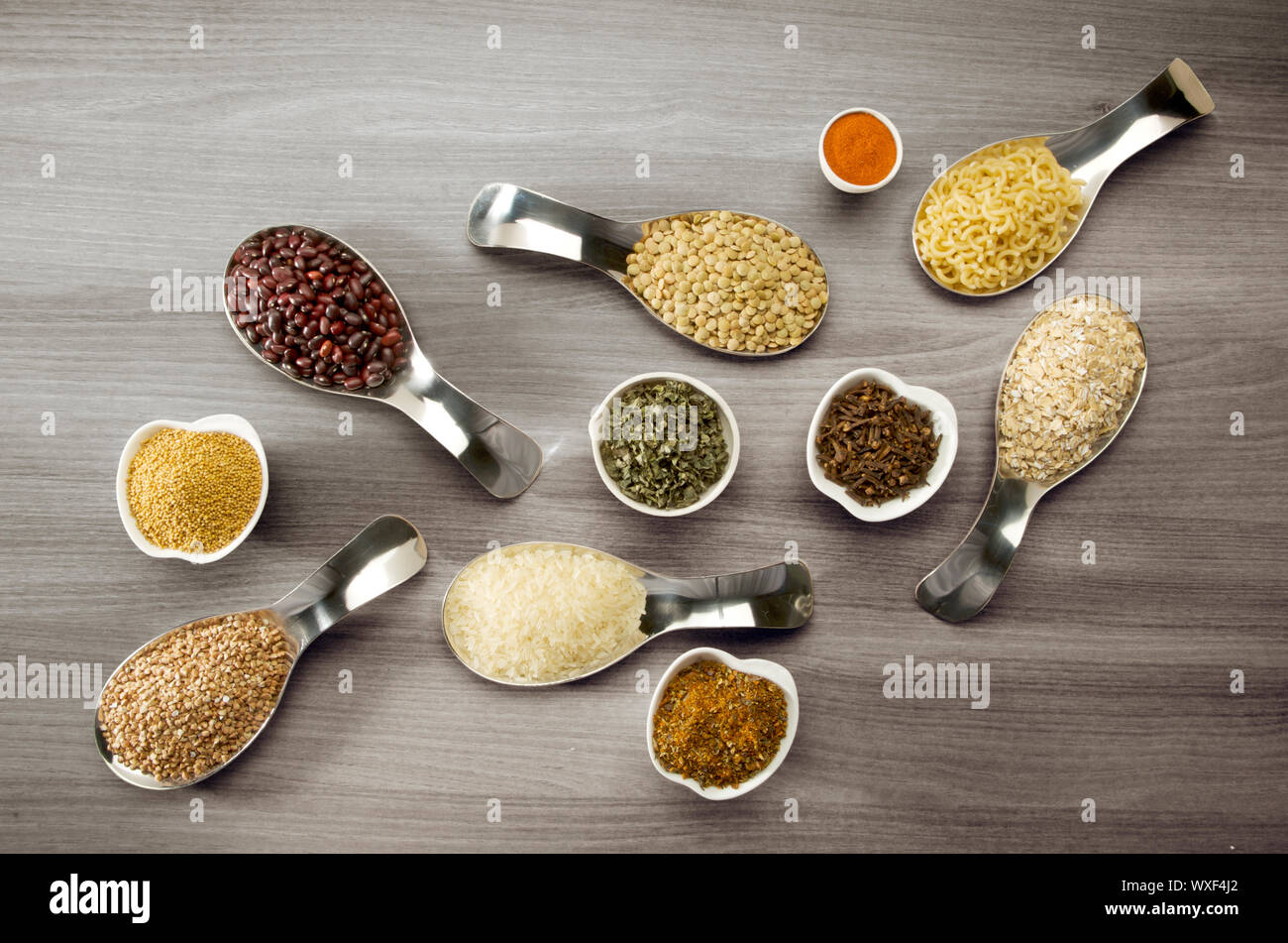 Chicchi di riso semi di grano saraceno lenticchie spezie in cucchiai su sfondo di legno Foto Stock