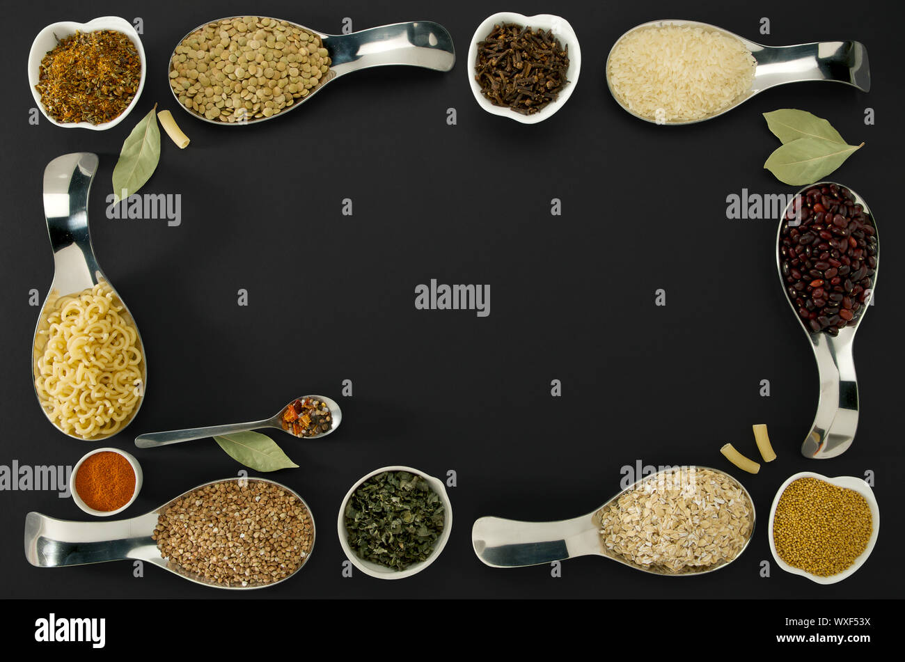 Chicchi di riso semi di grano saraceno lenticchie spezie in cucchiai su sfondo nero Foto Stock