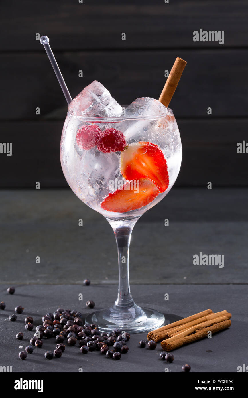Il gin tonic cocktail con Fragole Lamponi cannella e bacche di ginepro su  nero Foto stock - Alamy