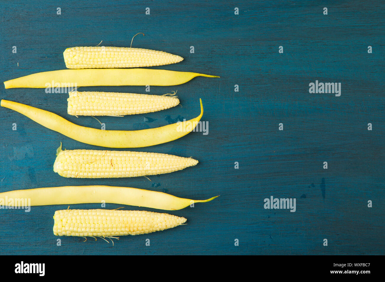 Il mais su una tavola di legno. I giovani giallo spighe di grano giacente sul blu scuro dello sfondo di legno. Cereali organici. Foto Stock
