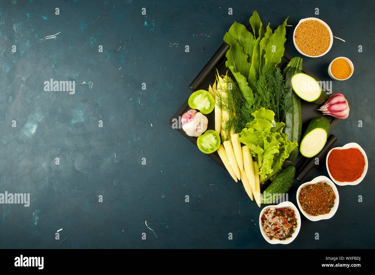 Le verdure in scatola sulla pietra uno sfondo scuro. Giovani Verdi aglio cipolla zucchine spezie luminose laici in un vassoio di legno Foto Stock