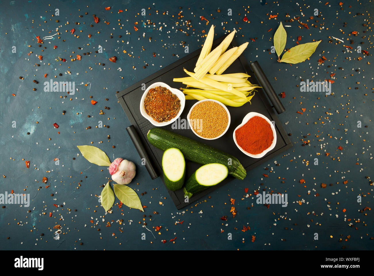 Le verdure in scatola sulla pietra uno sfondo scuro. Giovani Verdi aglio cipolla zucchine spezie luminose laici in un vassoio di legno Foto Stock