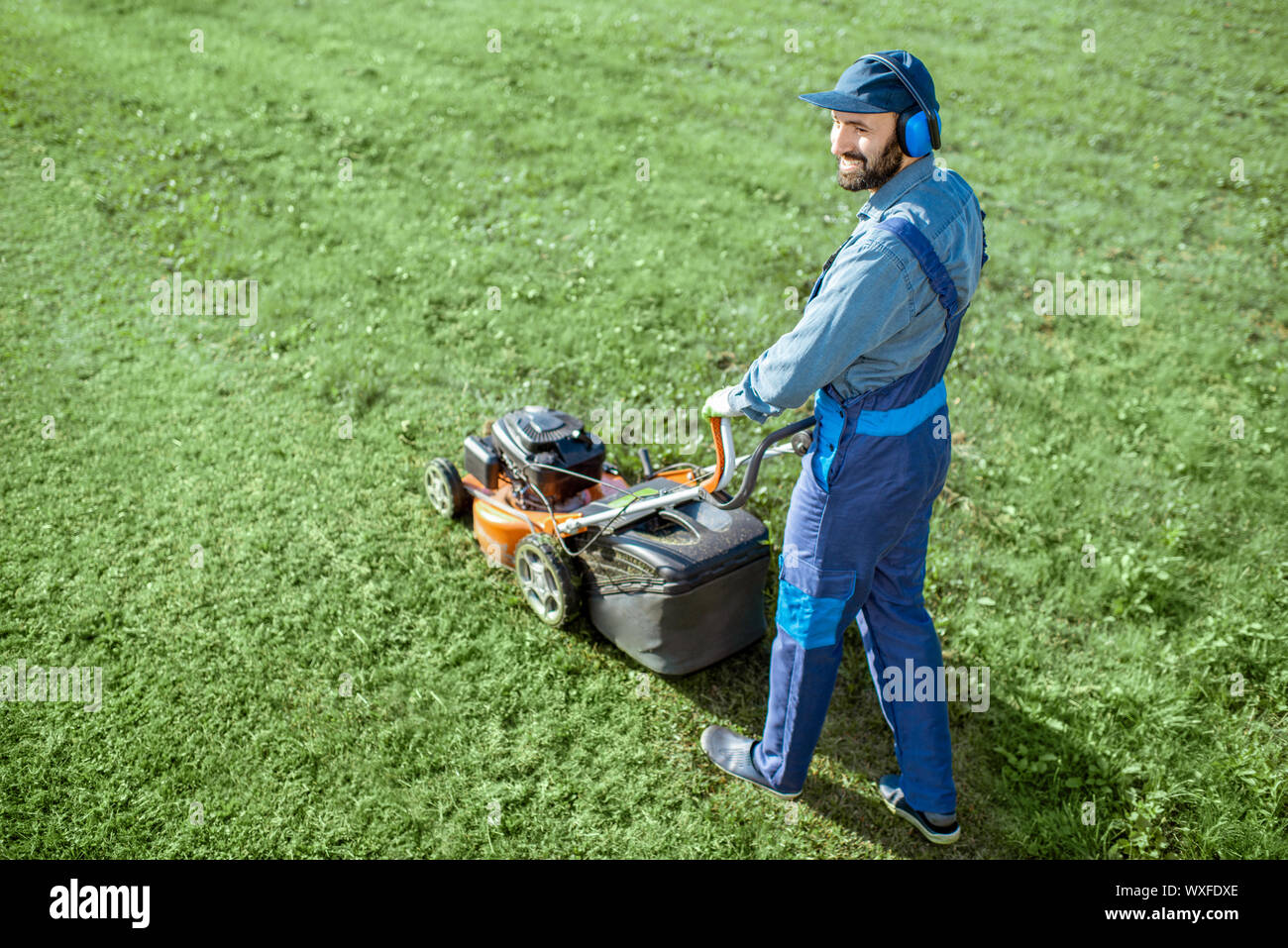 Professionale giardiniere di indumenti da lavoro protettiva taglio erba con benzina tosaerba sul cortile, vista da sopra Foto Stock