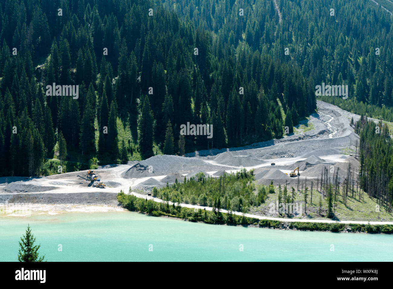 Escavatori e Pale gommate alla foce di un fiume di montagna spostare limo e sedimenti di roccia per constr Foto Stock