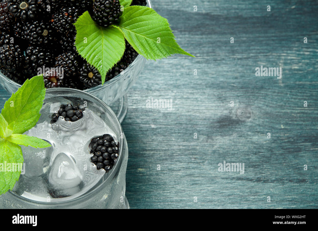 Blackberry fresco. Succosa di blackberry in una ciotola e un bicchiere di ghiaccio freddo acqua con frutti di bosco su un tavolo di legno. Vista da sopra. Copia Foto Stock